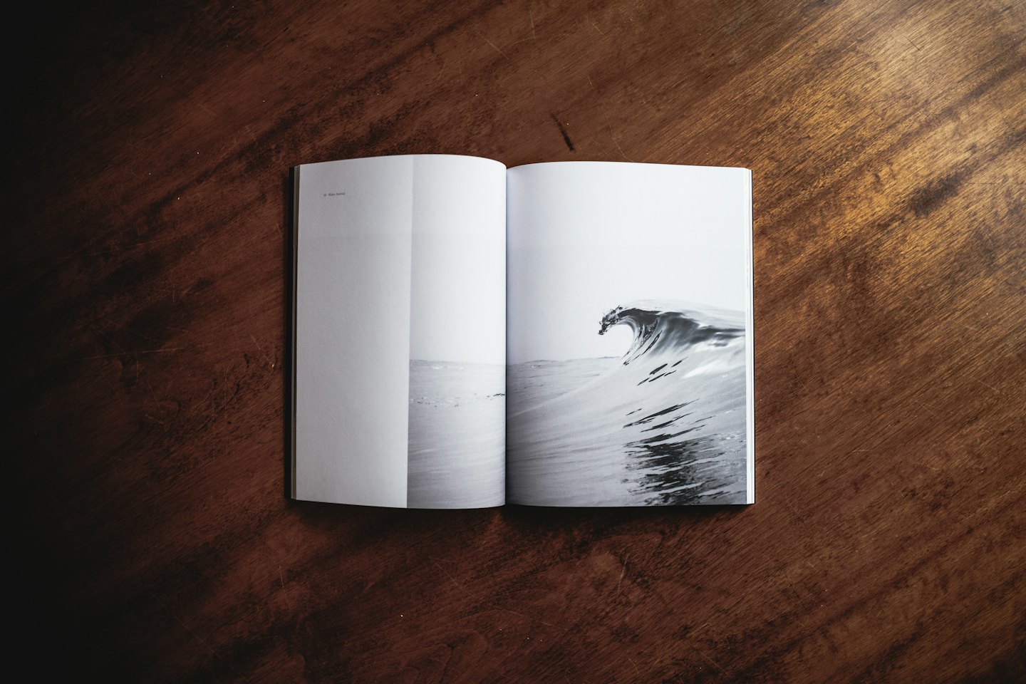 Rivista aperta su un tavolo di legno scuro con foto di un'onda dell'oceano.