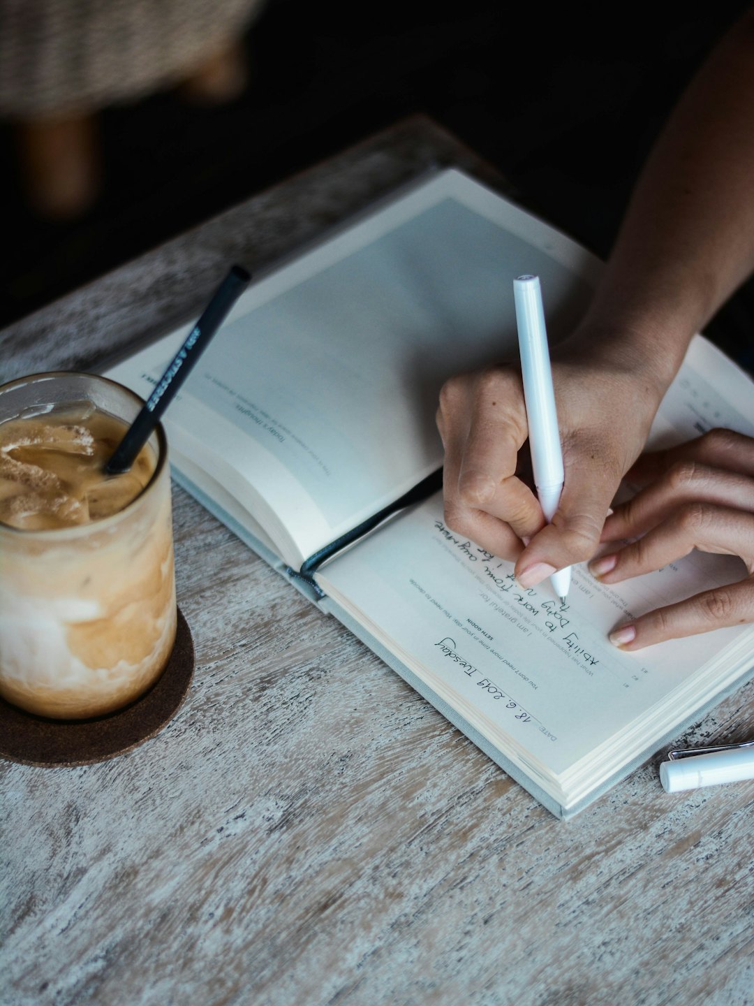 Mani che scrivono su un diario con un pennarello bianco e caffè freddo.