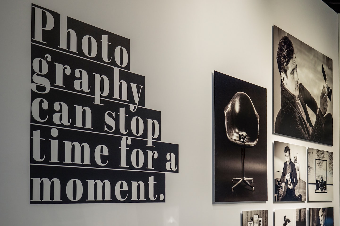 Parete di una galleria con testo grafico e fotografie incorniciate in bianco e nero.