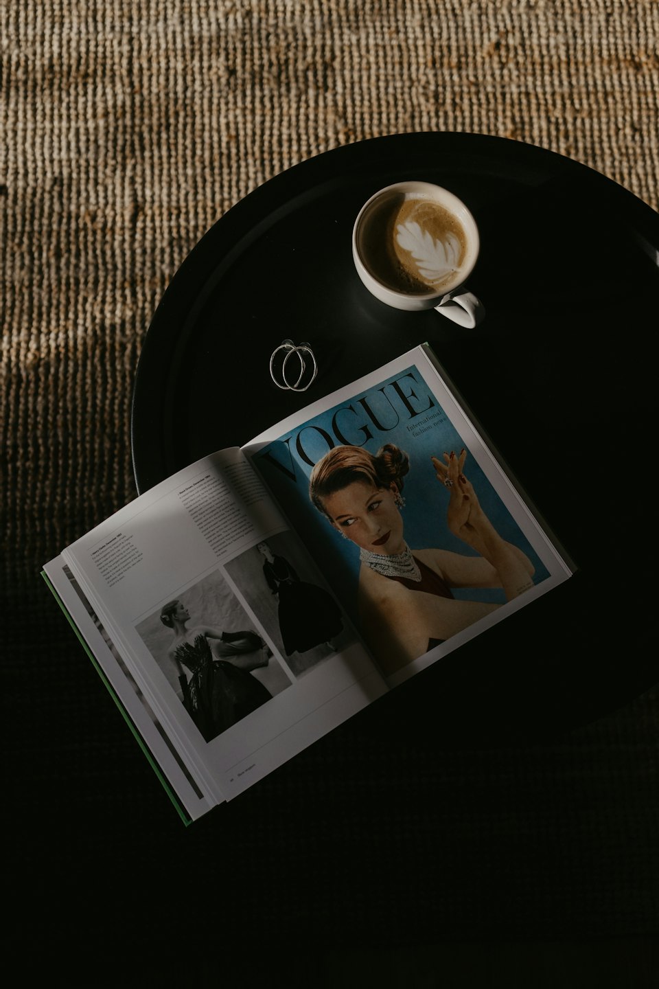 Rivista di moda aperta con caffè e orecchini su un tavolo.