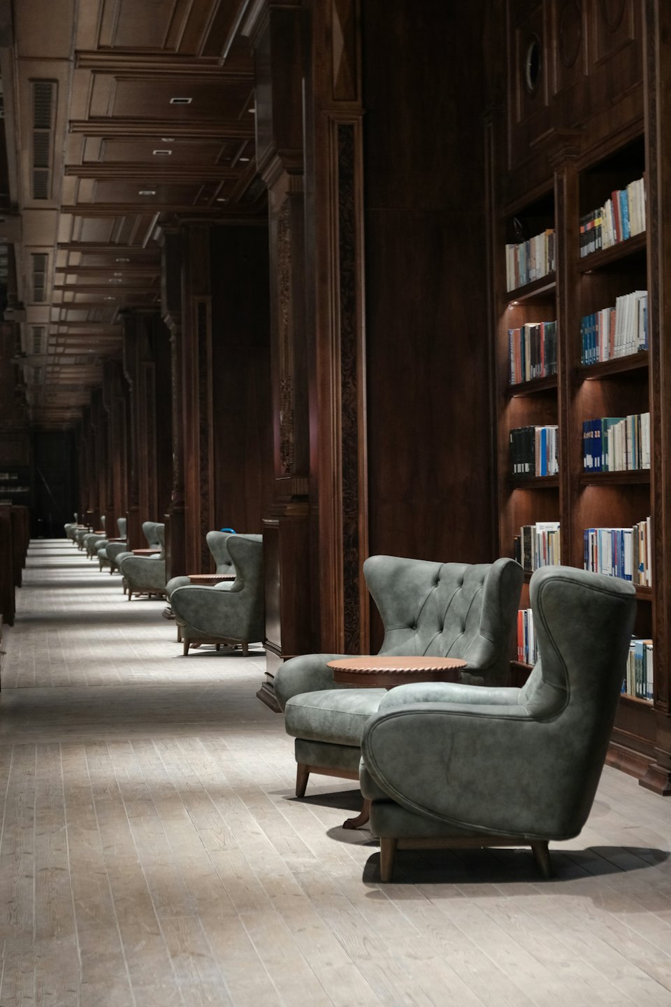 Poltrone verdi fiancheggiano una biblioteca con librerie e boiserie in legno.